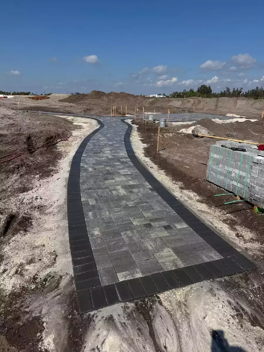 Curved gray concrete paver walkway with a dark border on a development lot in North Port, Florida