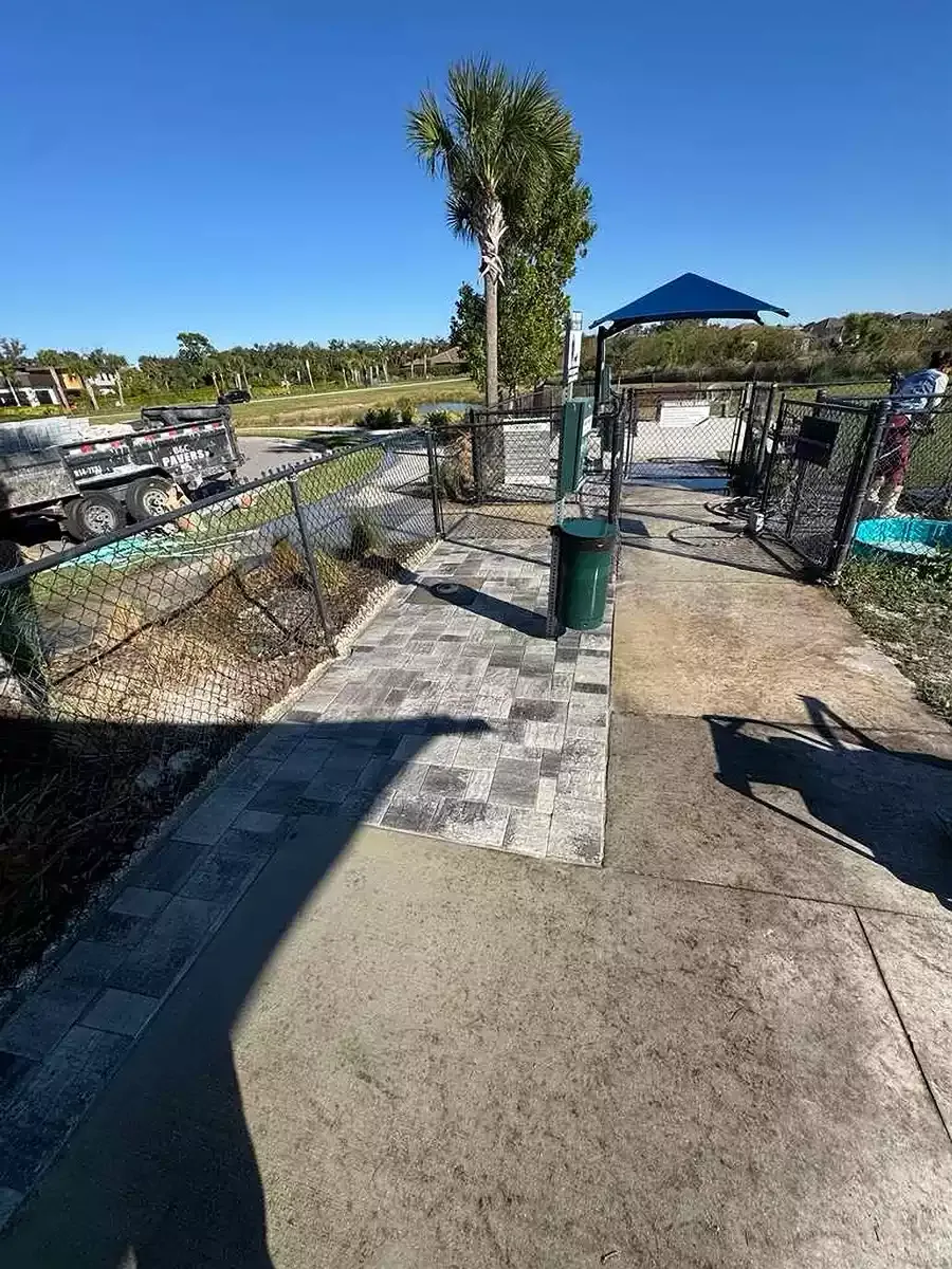 Gray concrete paver walkway beside a fenced commercial dog park entrance in Osprey, Florida